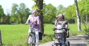 man in scootmobiel met vrouw op fiets
