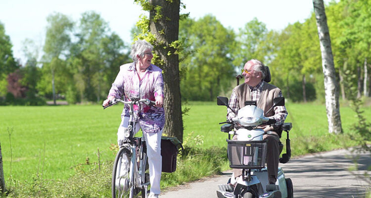 man in scootmobiel met vrouw op fiets